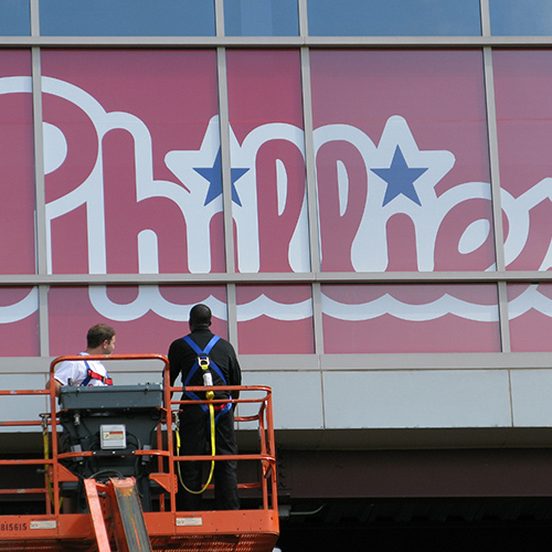 Two men on a boom lift installing a large Philadelphia Phillies logo.